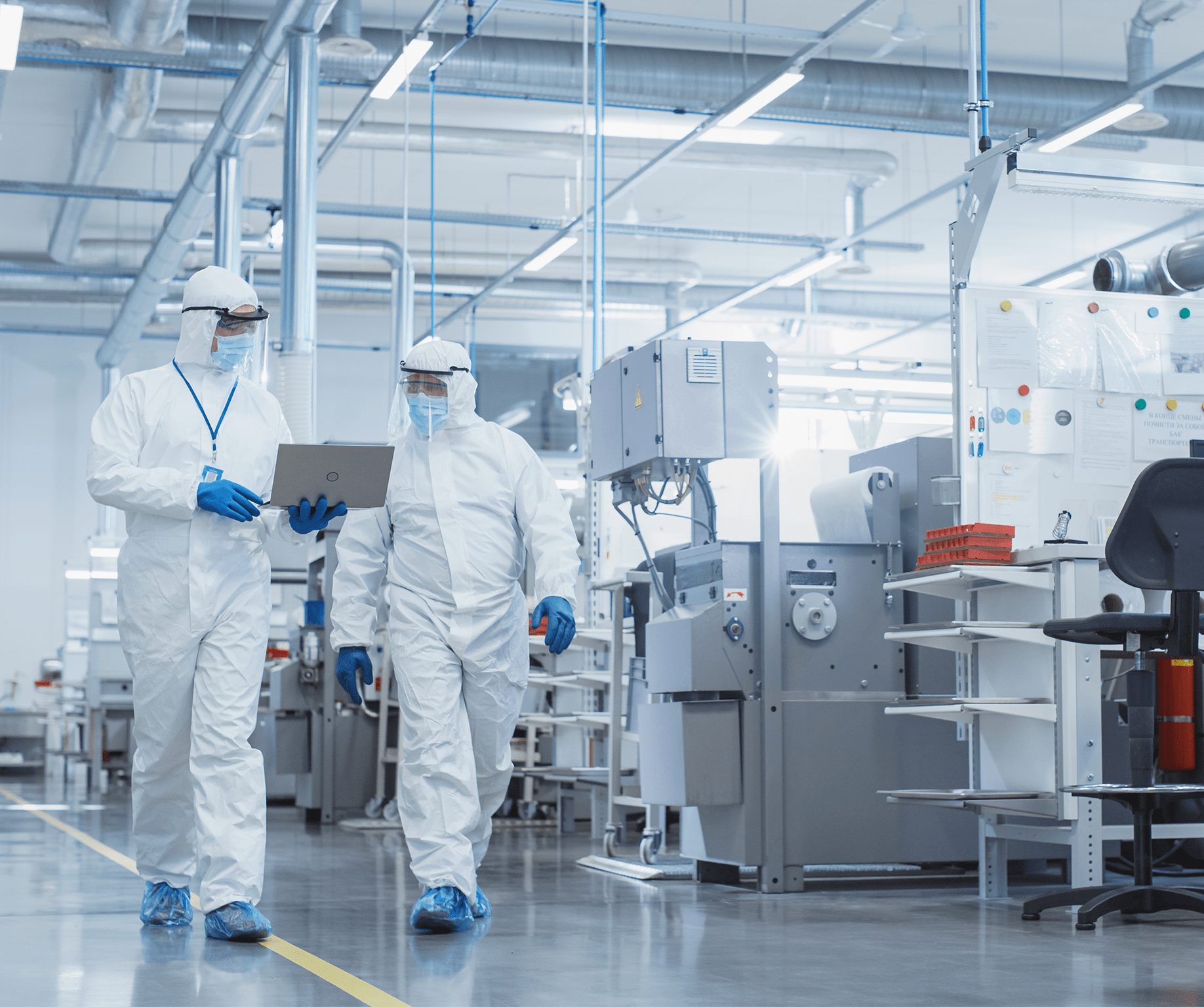 Two Scientists in Sterile Coveralls Walking in a Heavy Industry Factory with Laptop Computer,